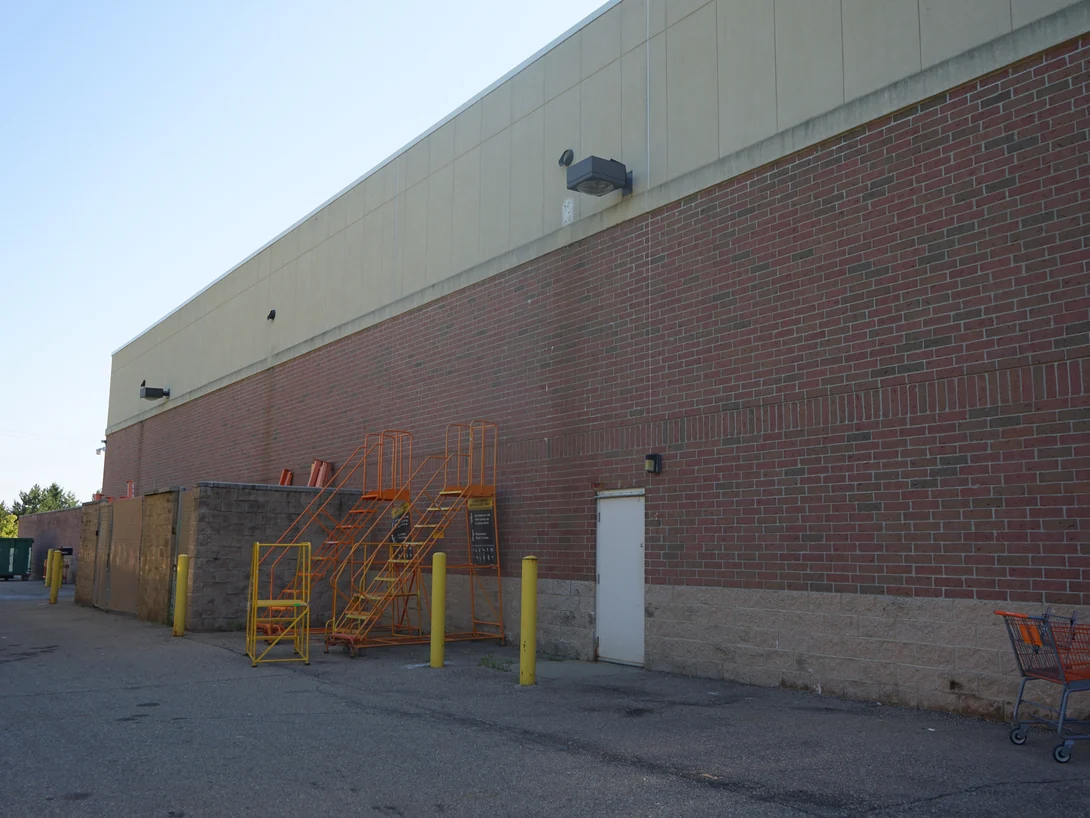 The service side of the store in 2019, red brick running the length of the wall above a cast stone base, with rolling ladders stacked by a service door