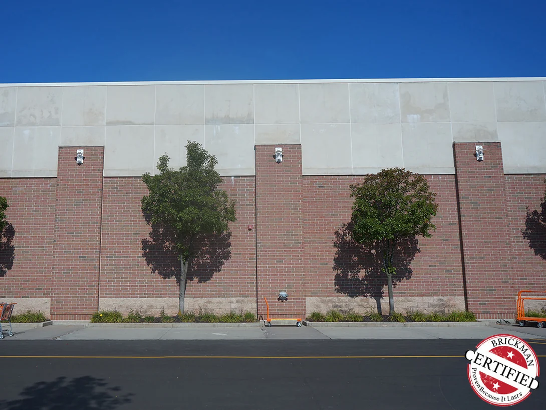 The frontage in 2019 seen across the car park, four bays of even red brick between planted beds and the parapet, the frame carrying the Brickman Certified stamp