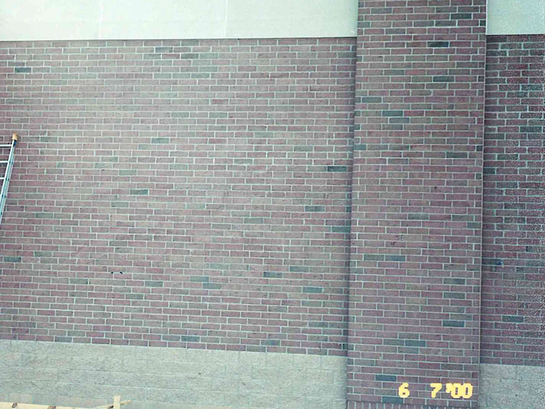A bay of new brick on the store wall in June 2000, the color running pale and uneven across the panel, a ladder leaning at the pilaster and bare ground at the base