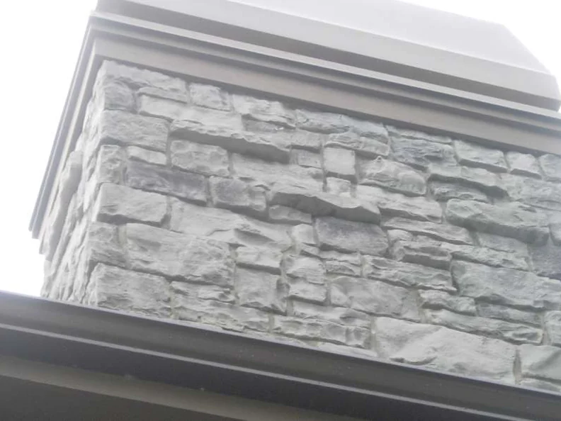The chimney in 2007, manufactured stone in a uniform pale grey and white under a wide cornice, seen from below past a gutter line