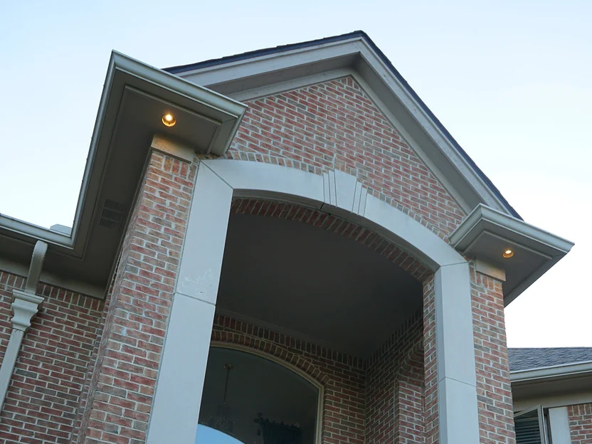 The gabled entry porch from below in 2019, a brick arch on cast stone piers with soffit lights either side and even red brick above