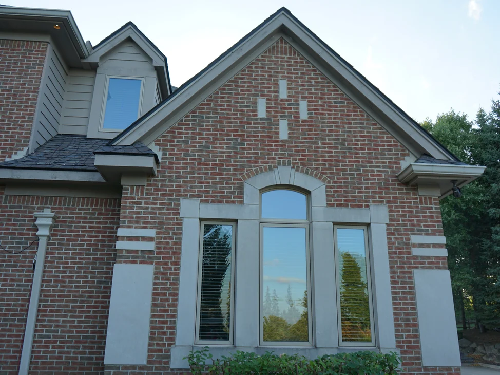 The gable end of the Michigan house in 2019, its brick an even red and brown range with cast stone blocks in the gable field and an arched window group below.