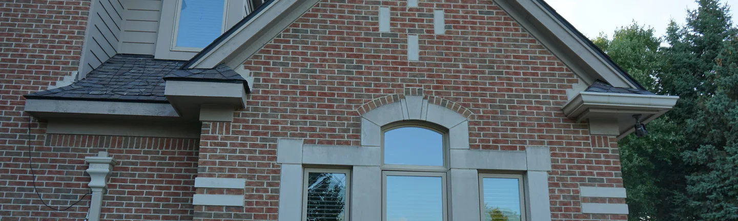 The brick gable of the Michigan house in 2019, an even red and brown range around an arched window with a cast stone surround