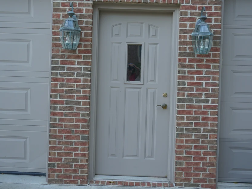 A service door between two garage bays in 2019, a lantern on each side and the brick pier and arched heads reading as one red and brown range