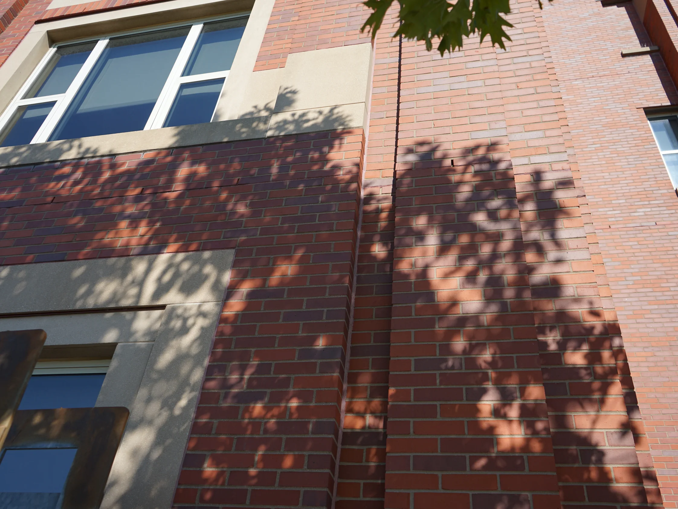 An outside corner of the hospital in 2019, tree shadows falling across red brick piers and cast stone banding