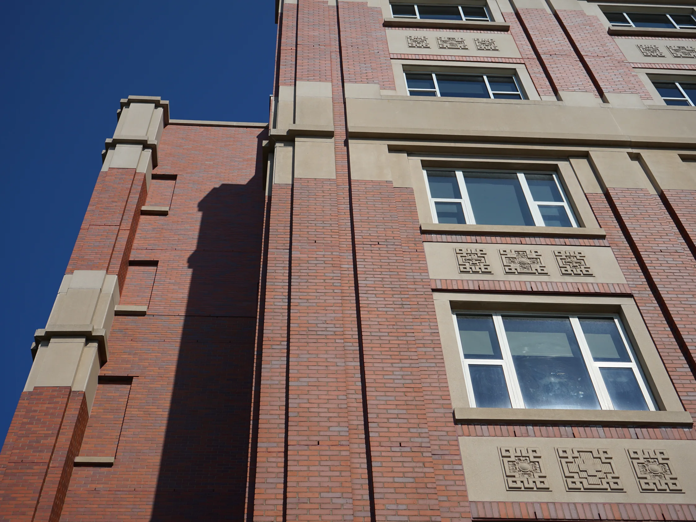 The upper floors of the hospital in 2019, red brick piers stepping past cast stone panels of geometric ornament under a clear sky
