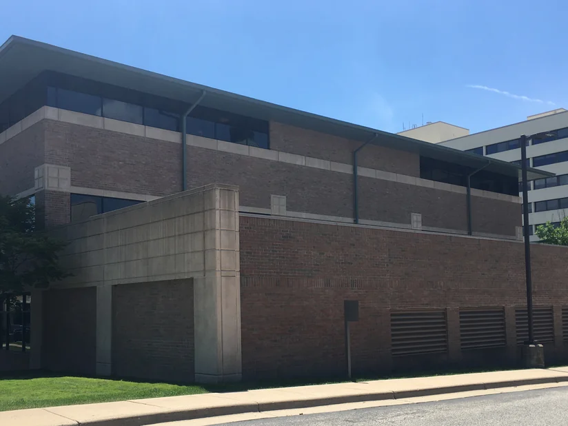 The hospital from the street in 2019, two storeys of brick over a cream precast screen wall, the brick holding one red range across both levels.