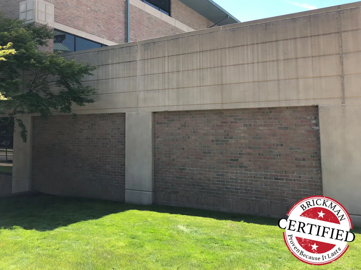 A panel of brick between precast piers on the lawn side of the hospital in 2019, the courses holding one red range, the frame carrying the Brickman Certified stamp
