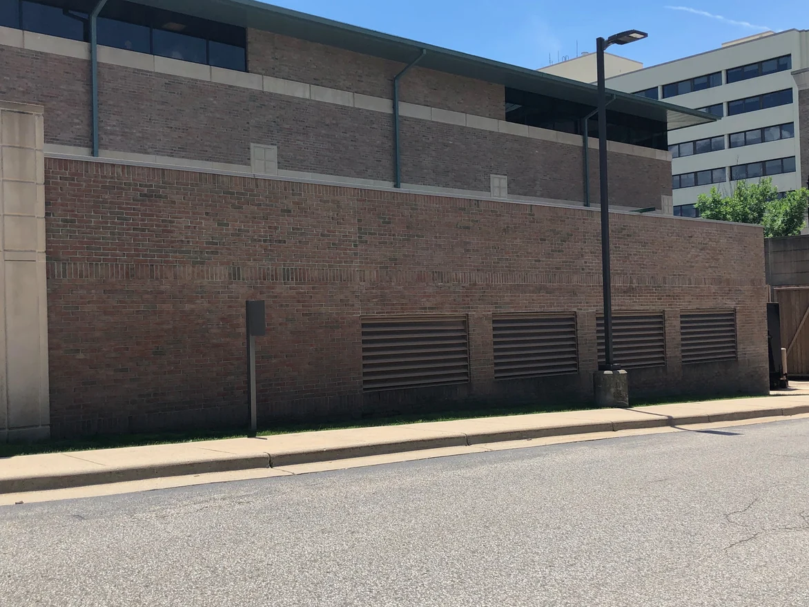 The long brick wall along the kerb in 2019, its courses even in color past four louvre vents to the far corner
