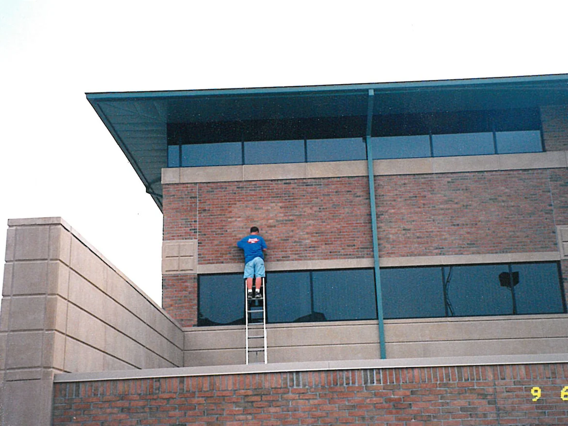 An applicator on a ladder working a panel of second storey brick on the hospital in 1998, the courses around him mixed red and pale tan