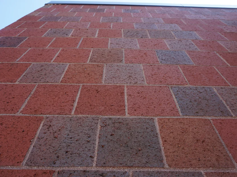 Looking straight up the wall of the addition in 2019, square textured units in reds and browns with pale mortar joints