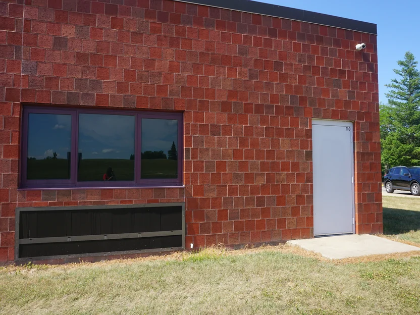 A window and a grey steel door on the addition in 2019, the brick around them a red range with darker units, a car parked on the drive beyond