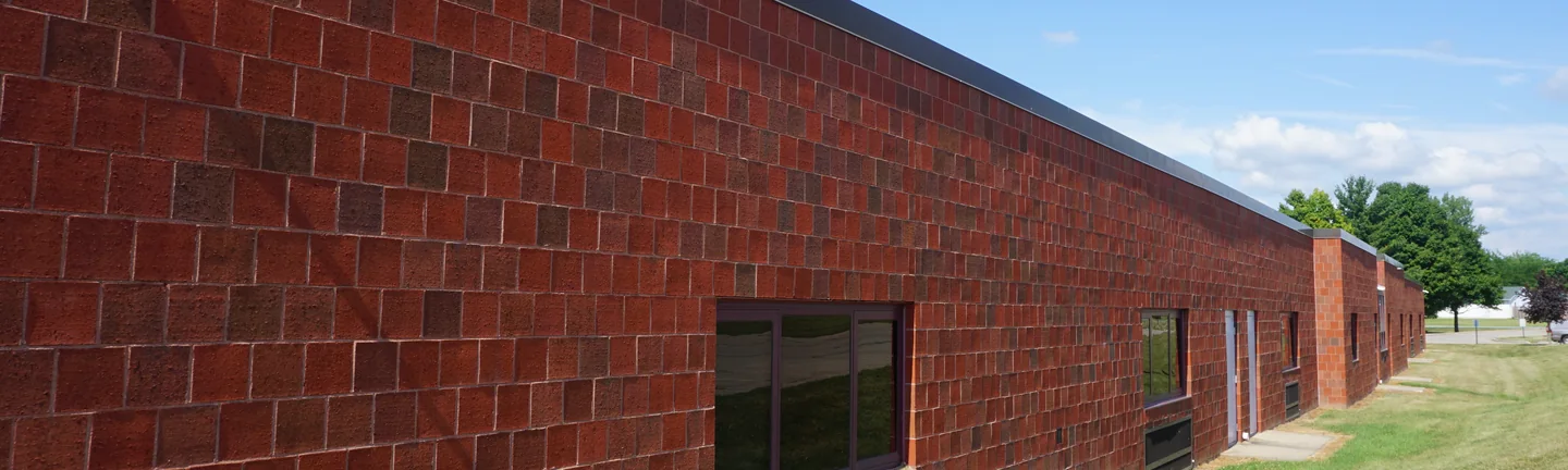 The long brick wall of the middle school addition in 2019, red units with darker ones scattered through the courses under a dark parapet
