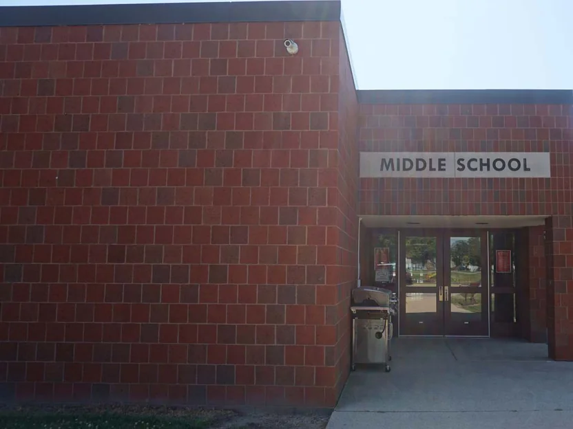 The middle school entrance in 2019, the wall of the addition meeting the original entrance bay and its MIDDLE SCHOOL sign, a grill parked beside the doors
