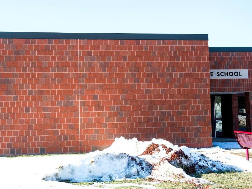 The same wall after staining, labelled 2001 in the file, the units now one red range under a dark parapet, with a pile of snow on the lawn and the entrance sign beyond