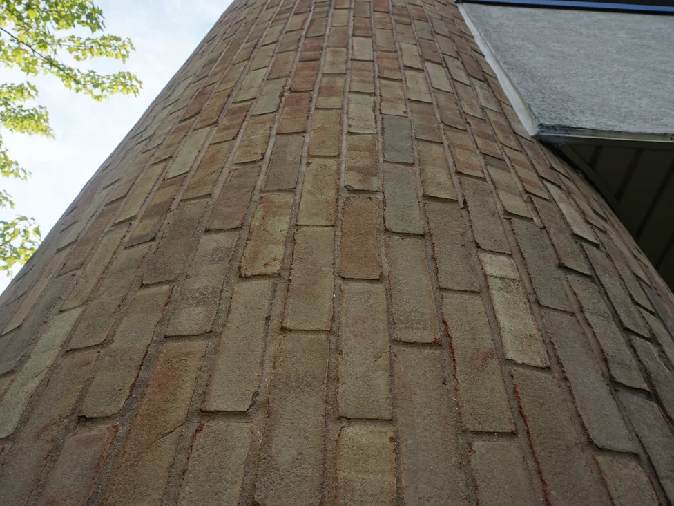 Close view up the curved brick pier in 2019, the units in mixed tan, buff and dull red with deep raked mortar joints