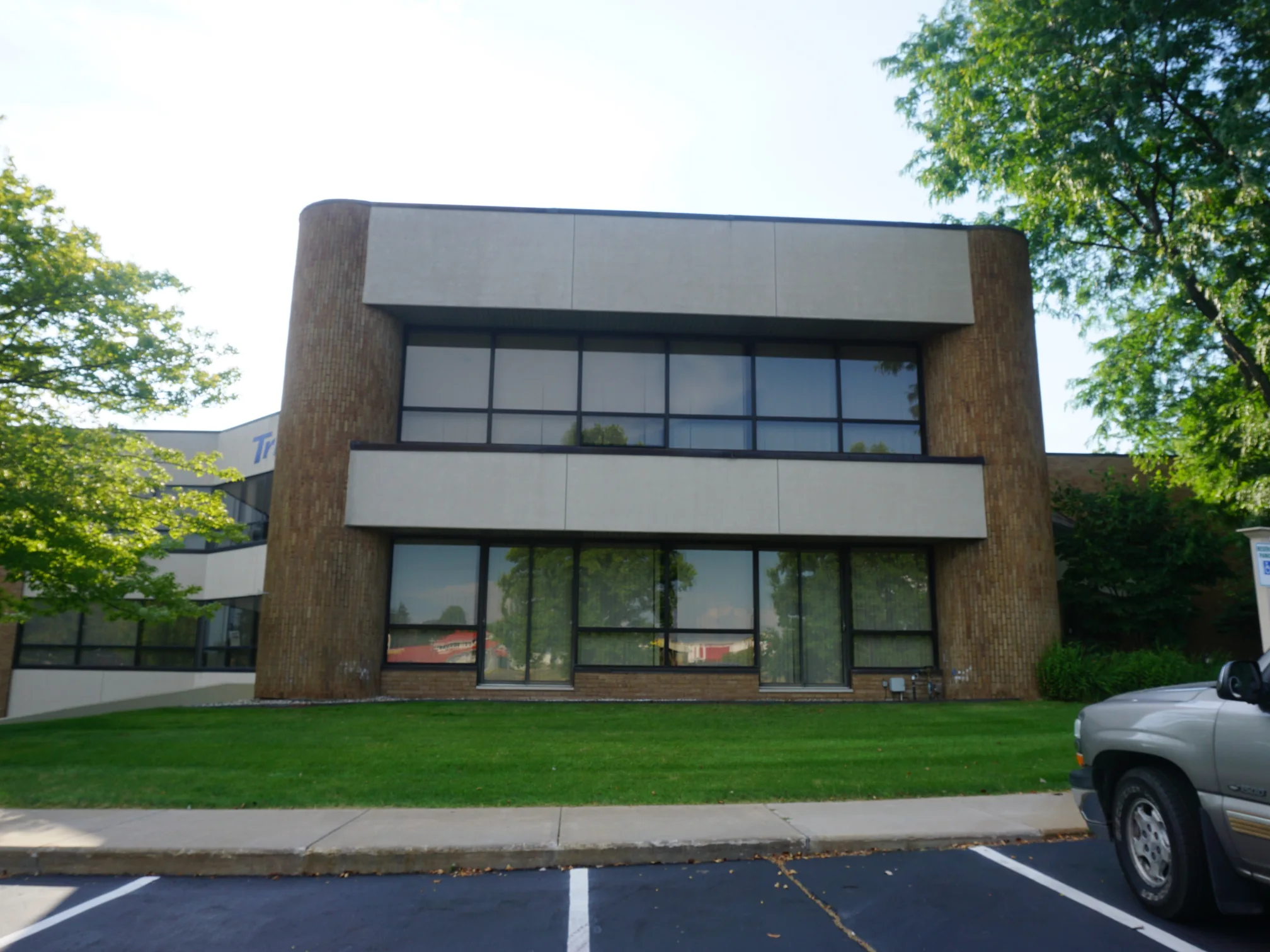 The two-story office from the car park in 2019, one tan and buff brick range running around the rounded corner pier at each end of the elevation