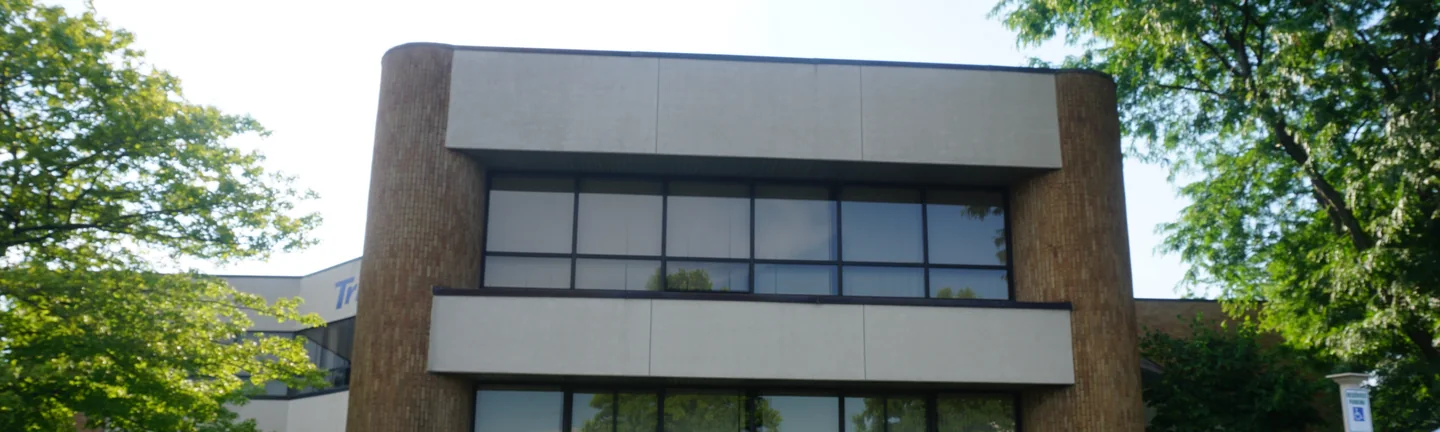 The Michigan office in 2019, tan brick running between beige spandrel bands and around the rounded corner piers at each end