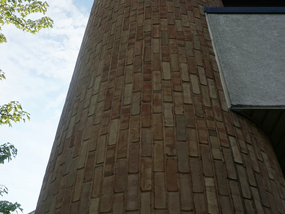The rounded brick corner of the office seen from the ground in 2019, running two stories to the roof edge past the beige spandrel band
