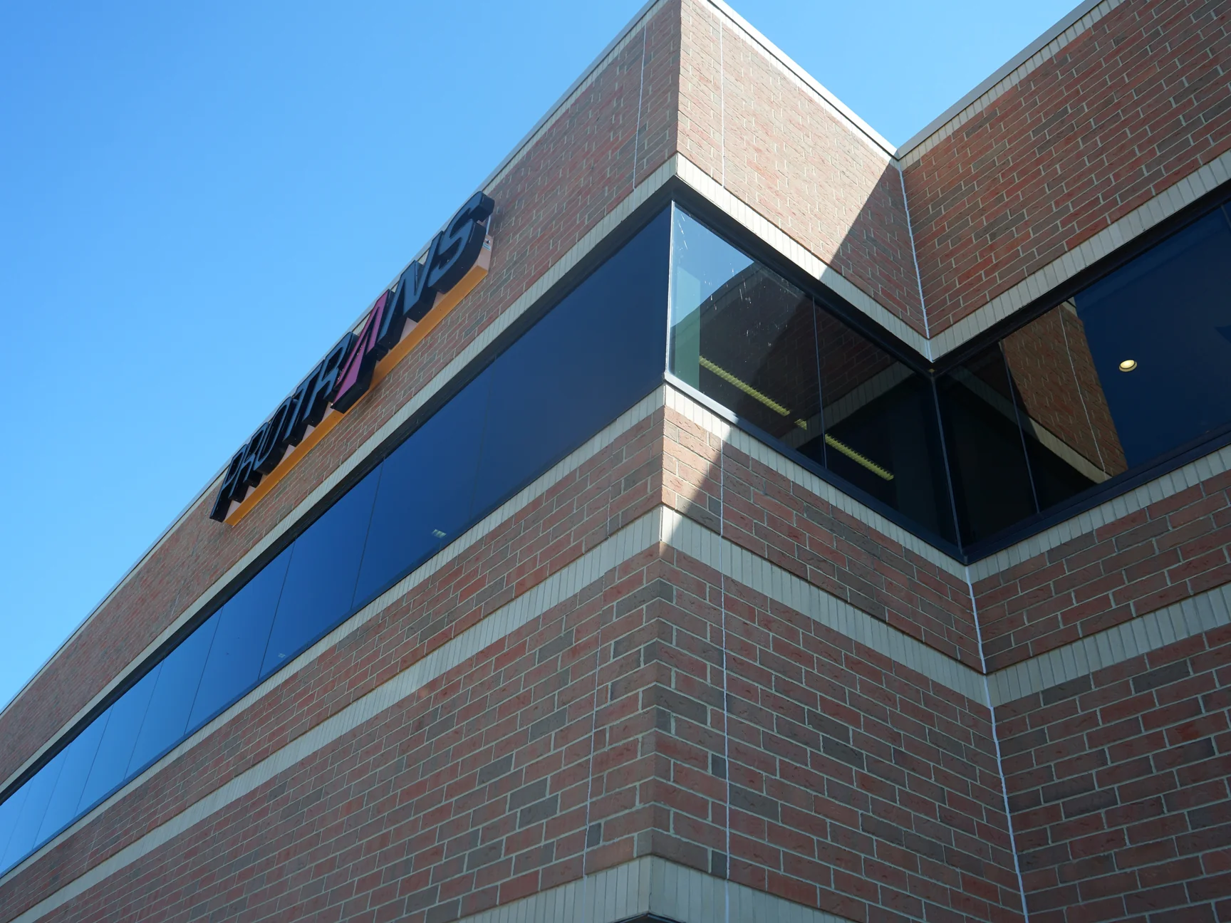 The office corner in 2019 under a clear sky, the brick reading as one even red and tan range across both faces