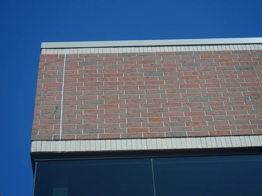 The top of a blended brick wall against a deep blue sky, red, tan and grey units mixed evenly below the stone coping