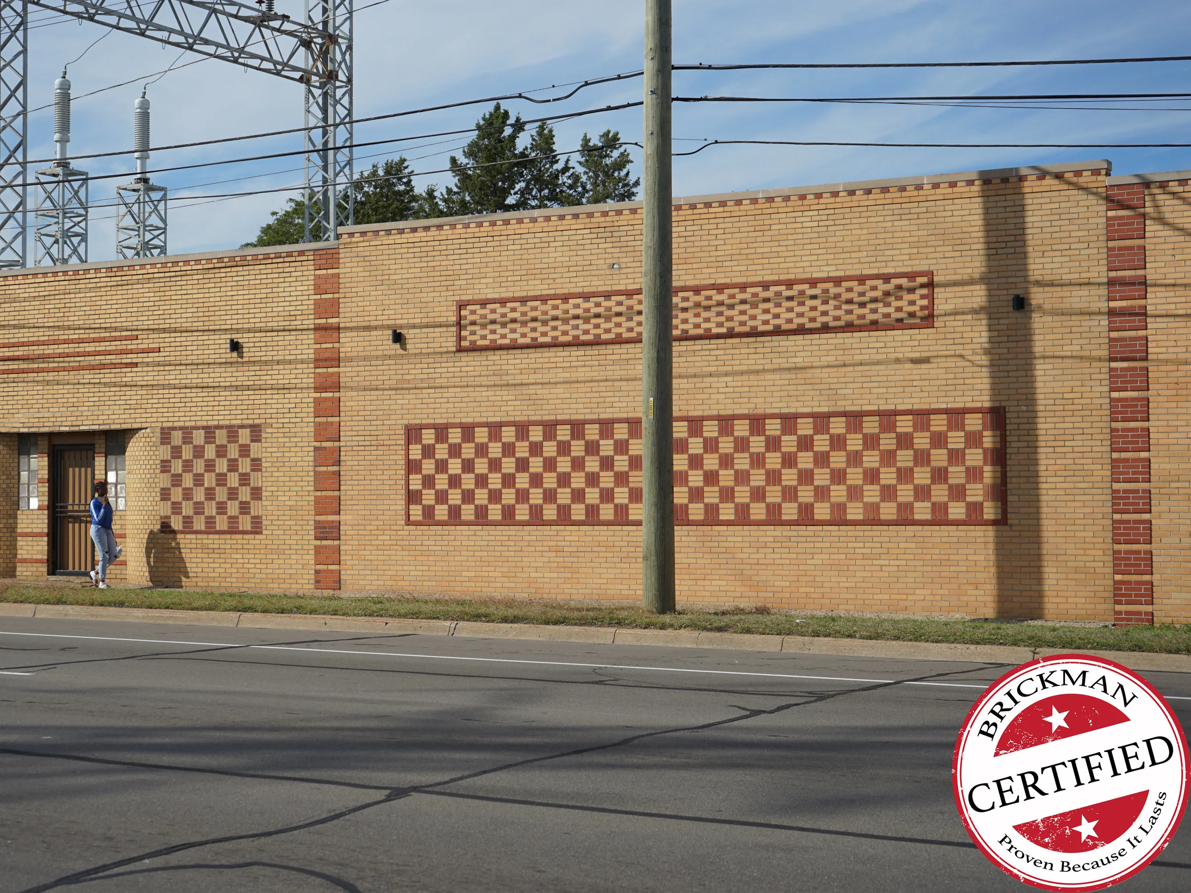 The office wall from across the road in 2019, its basketweave and checker panels reading as strong red against buff brick, with a certification stamp in the corner