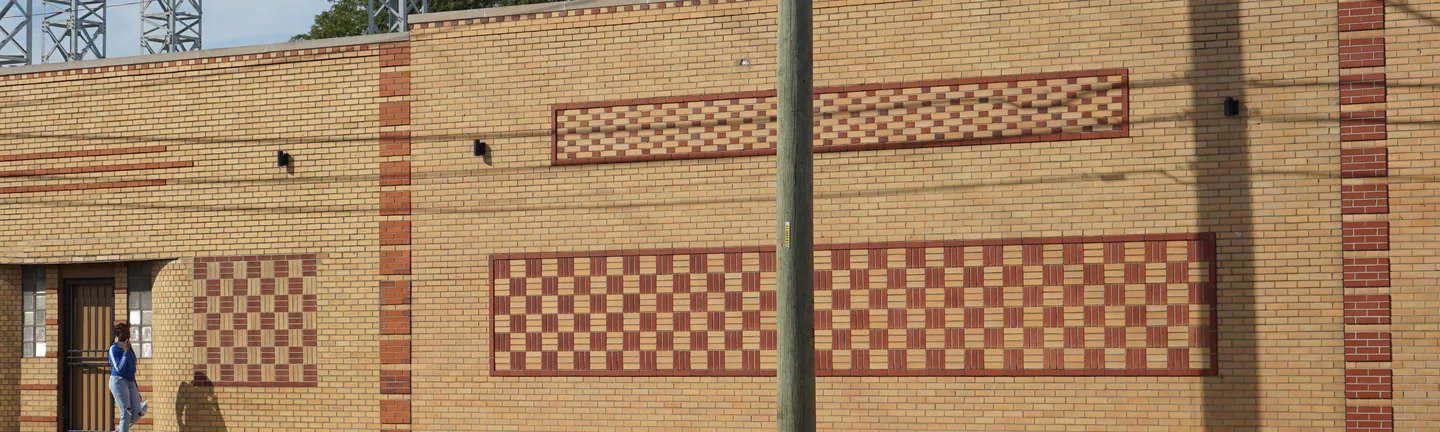 Buff brick wall carrying broad panels of red and buff basketweave and checker coursing