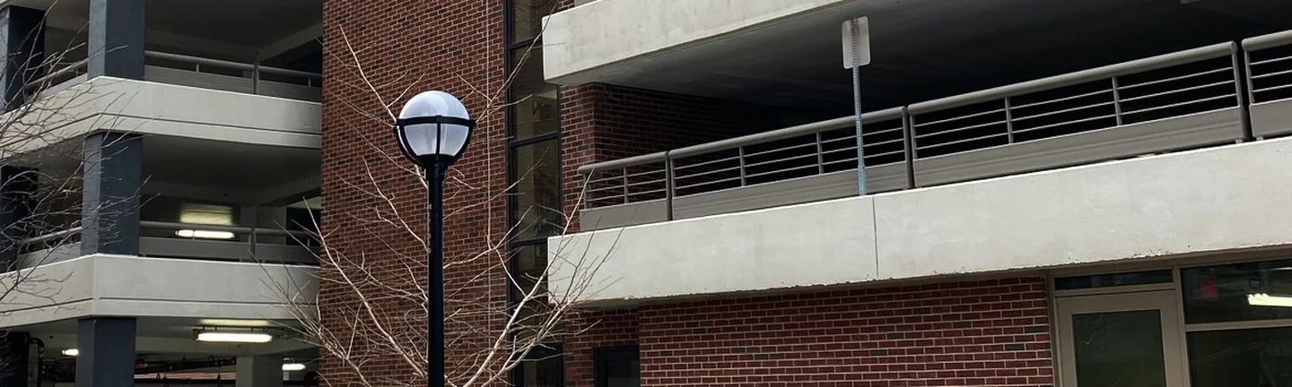 The red brick tower of the parking garage in 2020 between two blocks of open concrete decks, a lamp post and a bare tree in front of it