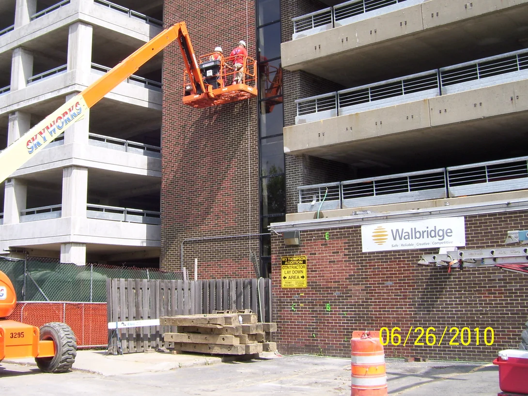 Two applicators in a lift basket against the brick tower of the parking garage in June 2010, the courses above them already red and the courses below still dark brown, open concrete decks on either side