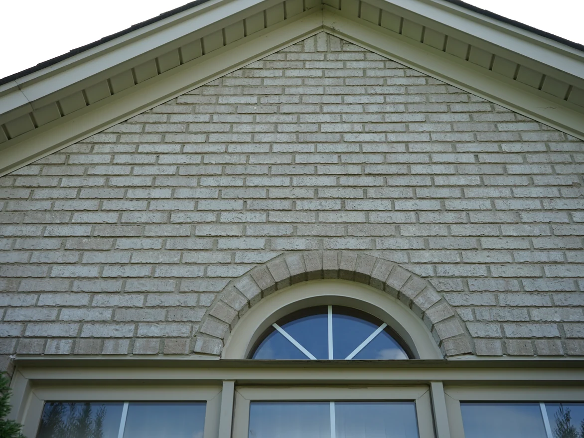 Close view of the gable brick in 2019, the arched header course over the window reading in the same cream range as the field around it