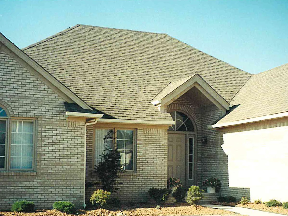 The front of the newly built house in 1999, cream brick above a bare dirt yard, with an arched window in the left gable and a gabled entry porch