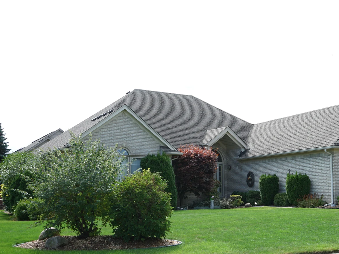 The house from the street in 2019, the main roof and both front gables standing above mature planting and a clipped lawn