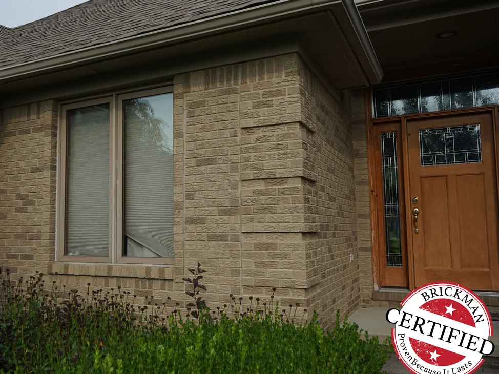 The front entry of the house in 2019, the rock-faced brick running from the window wall around the corner to the wood door as one tan range.