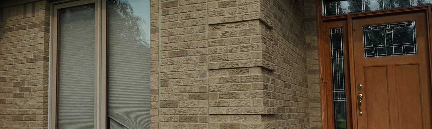 The front entry of the single-story house in 2019, its rock-faced tan brick running unbroken around the corner to the door