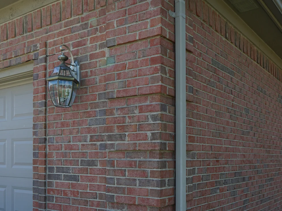 An outside corner of the house beside the garage door in 2019, a carriage lantern on the brick and the color consistent across both faces