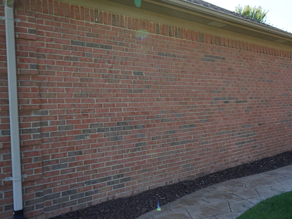 A long wall of the house in 2019 under a low hipped roof, the brick one even red range beside a stamped concrete walkway.