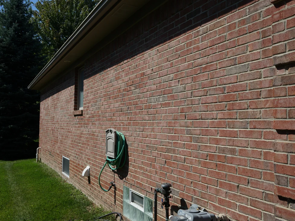 A side elevation of the house in 2019 seen along the wall, the brick even in color from the basement windows up to the eaves