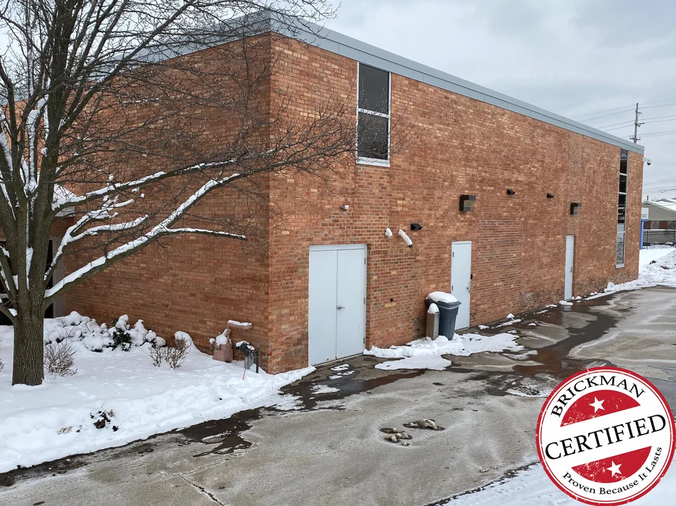 The corner of the Michigan building in 2021 with snow on the ground, red brick running as one range along the long wall past three doors, with the certification stamp in the corner