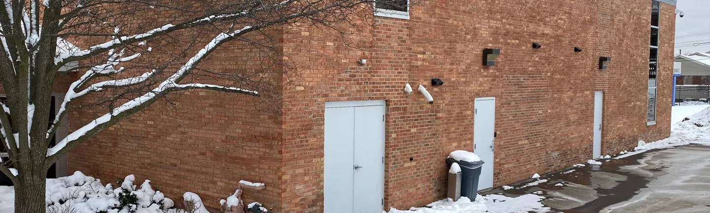 The corner of the Michigan building in 2021, red brick running as one range along the long wall past three doors