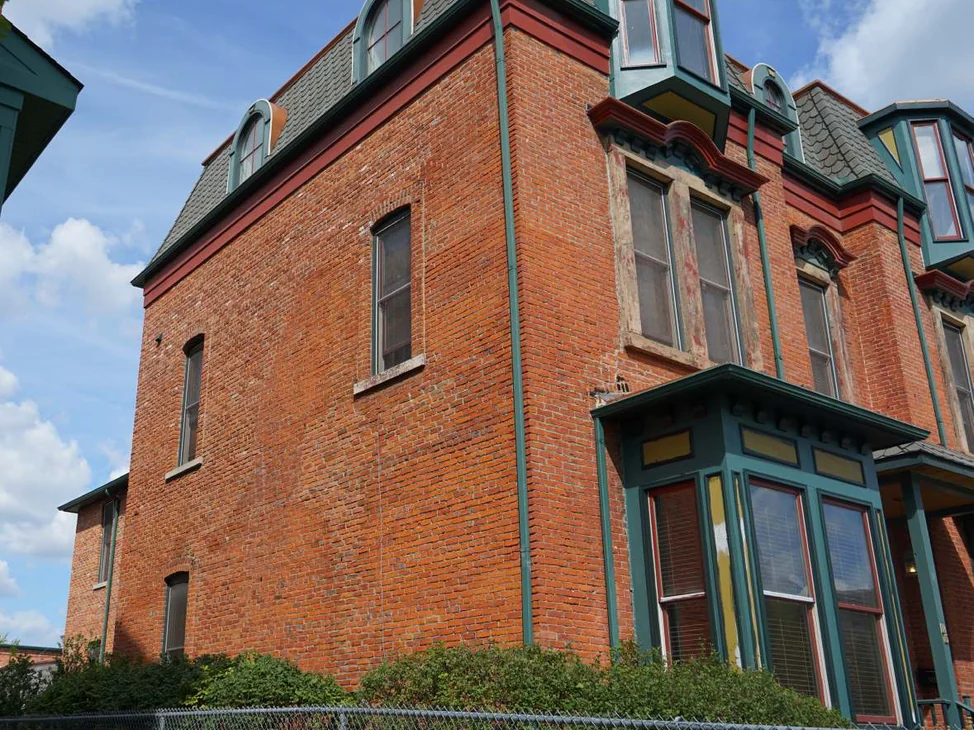 The corner of the Michigan home in 2019, one range of red brick running from the plain side wall round onto the front bays under a slate mansard roof