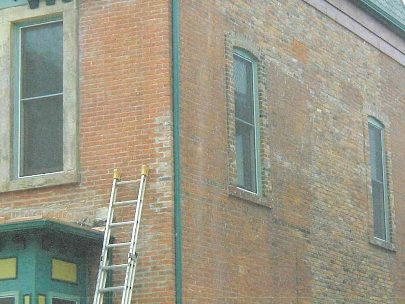 The corner of the house part way through the work in 2002, an extension ladder against the wall, the return to the left already an even red and the side wall beside it still mottled tan, olive and grey