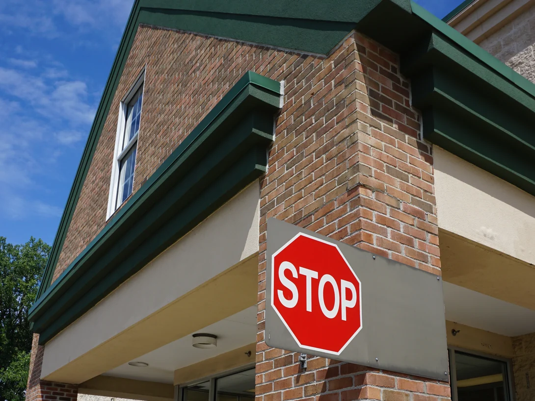 An entrance column in 2019 carrying a stop sign, its brick reading with the gable wall and the cast stone base behind it