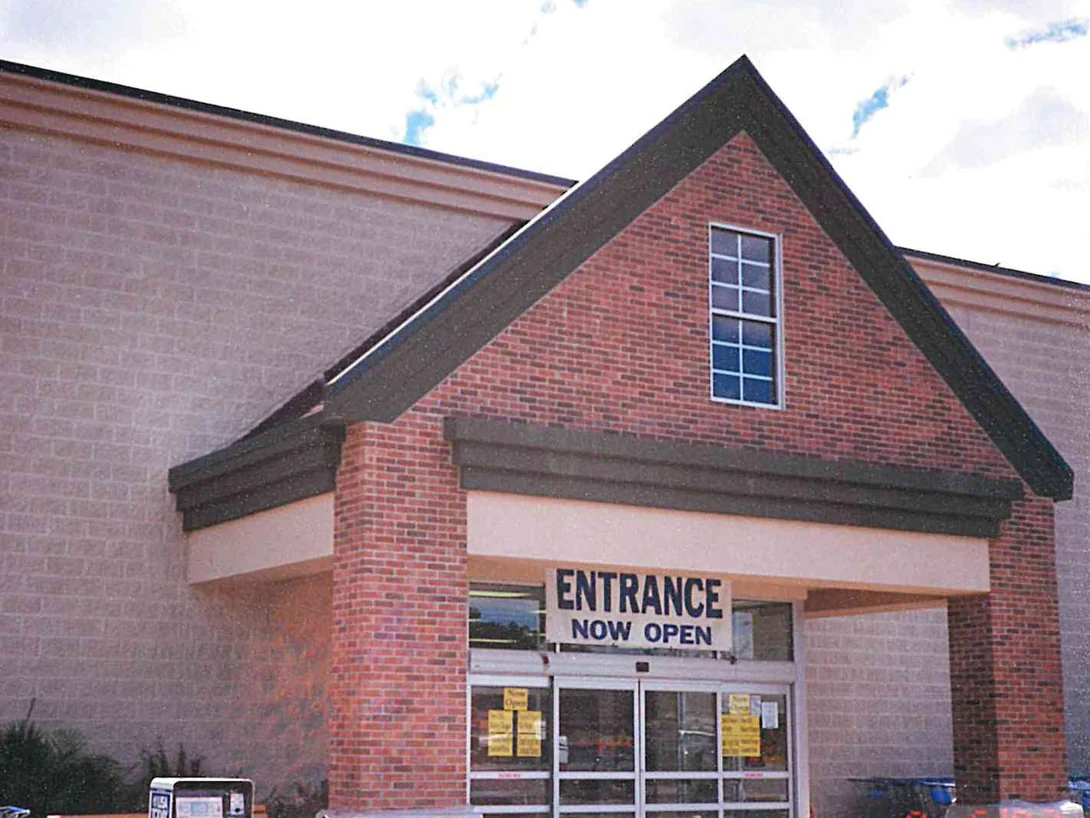 The store entrance in 1997 after staining, the gable and its columns reading as one red brown range beside the buff block wall