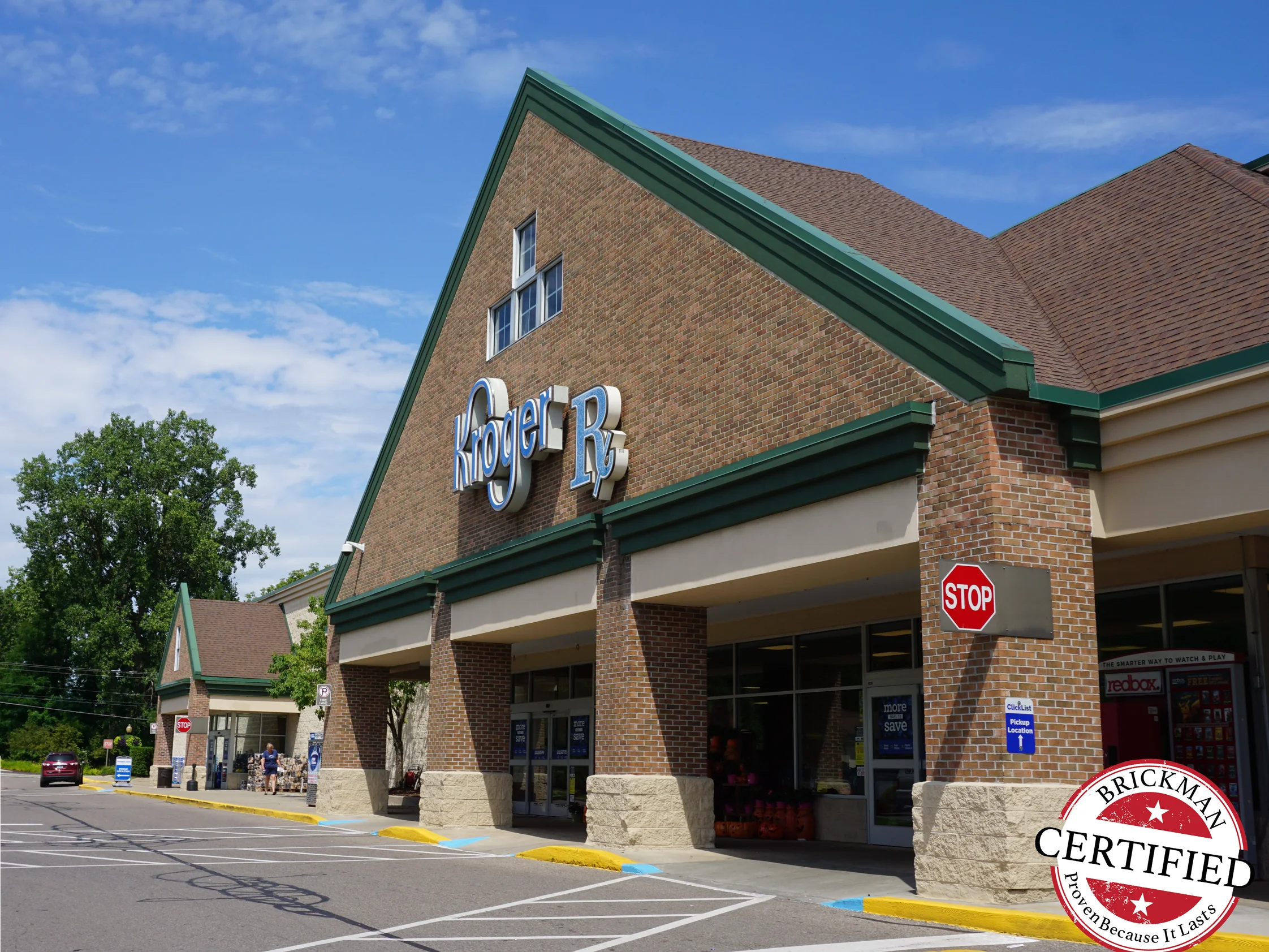 The front of the Kroger in 2019, its gabled brick entrance and columns running along the parking lot under a green cornice
