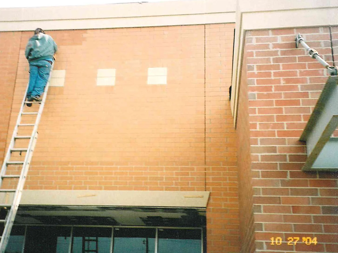 An applicator on an extension ladder at the top of the wall in 2004, the brick above the canopy a pale washed tan against the deeper red of the courses below it and of the pier alongside