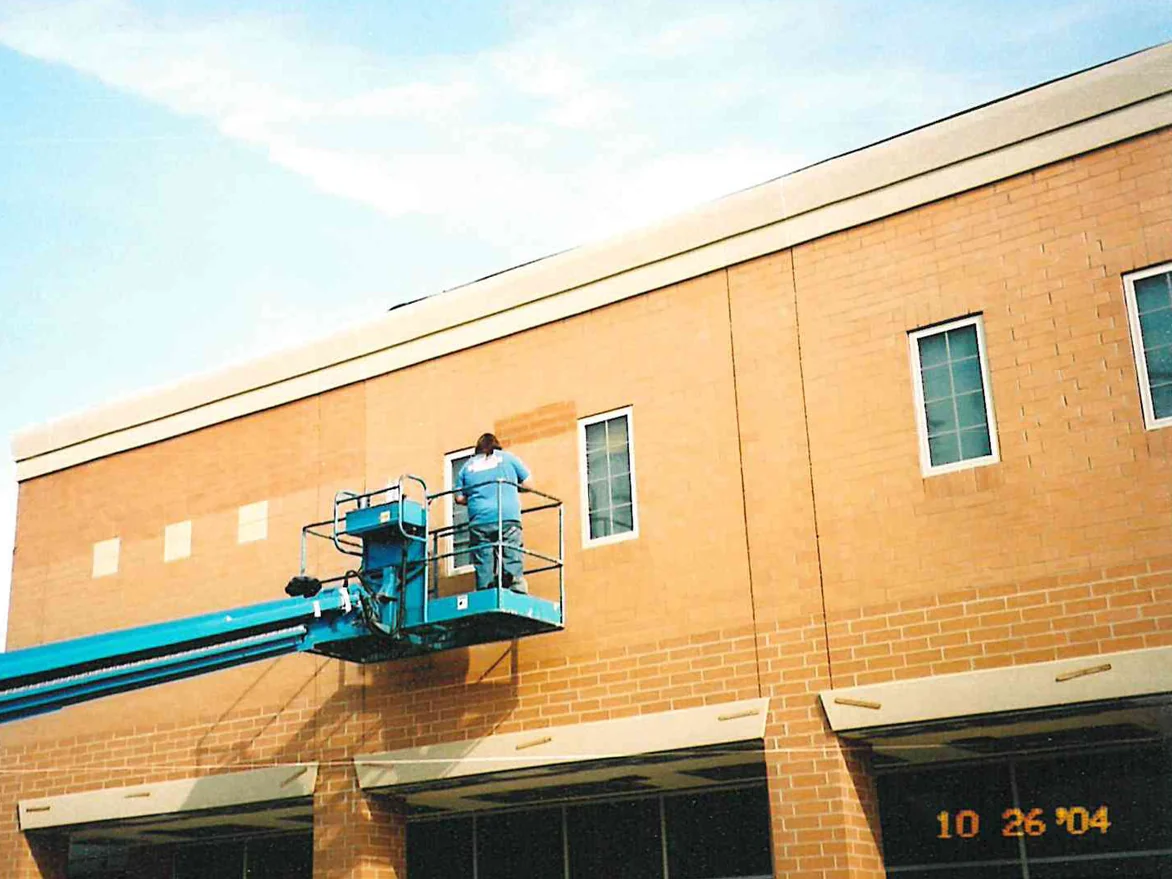 An applicator working from a boom lift along the upper wall of the plaza in 2004, a darkened patch of brick beside him against the lighter wall still to be reached