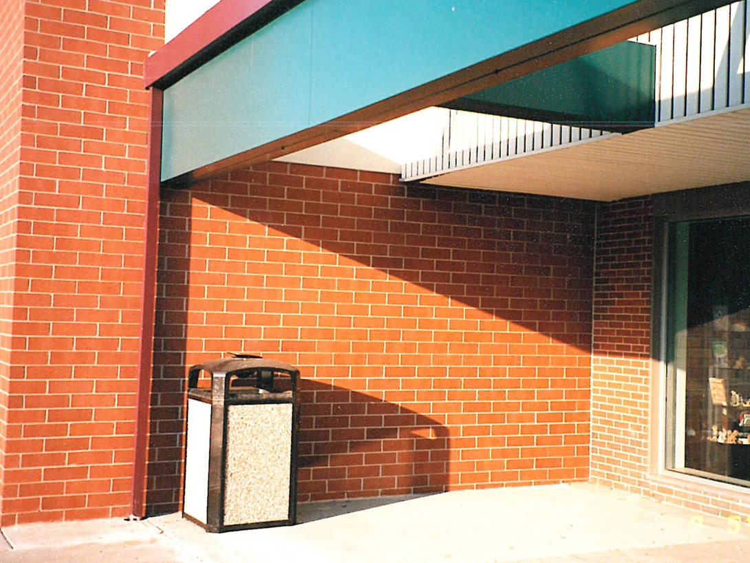 An inside corner of the walkway in 1998, red brick running from a pier past a bin to a shopfront window under the canopy