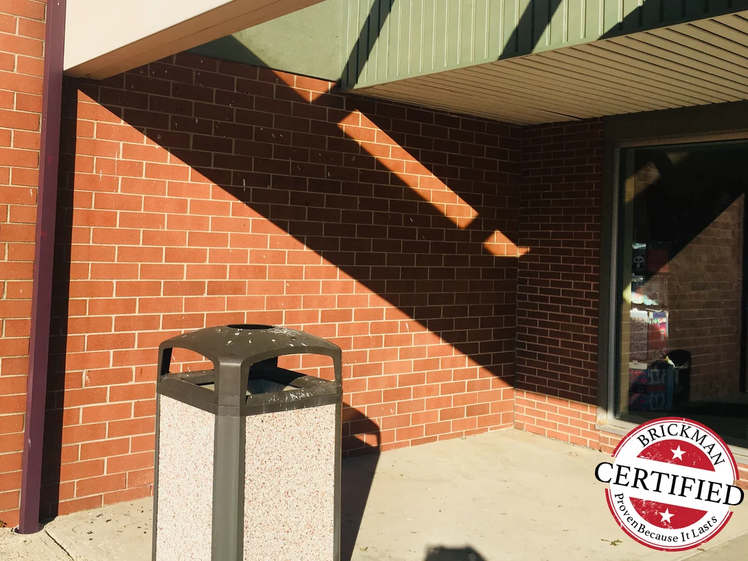 The same inside corner in 2019, the brick even from the pier past the bin to the shopfront window, the frame carrying the Brickman Certified stamp