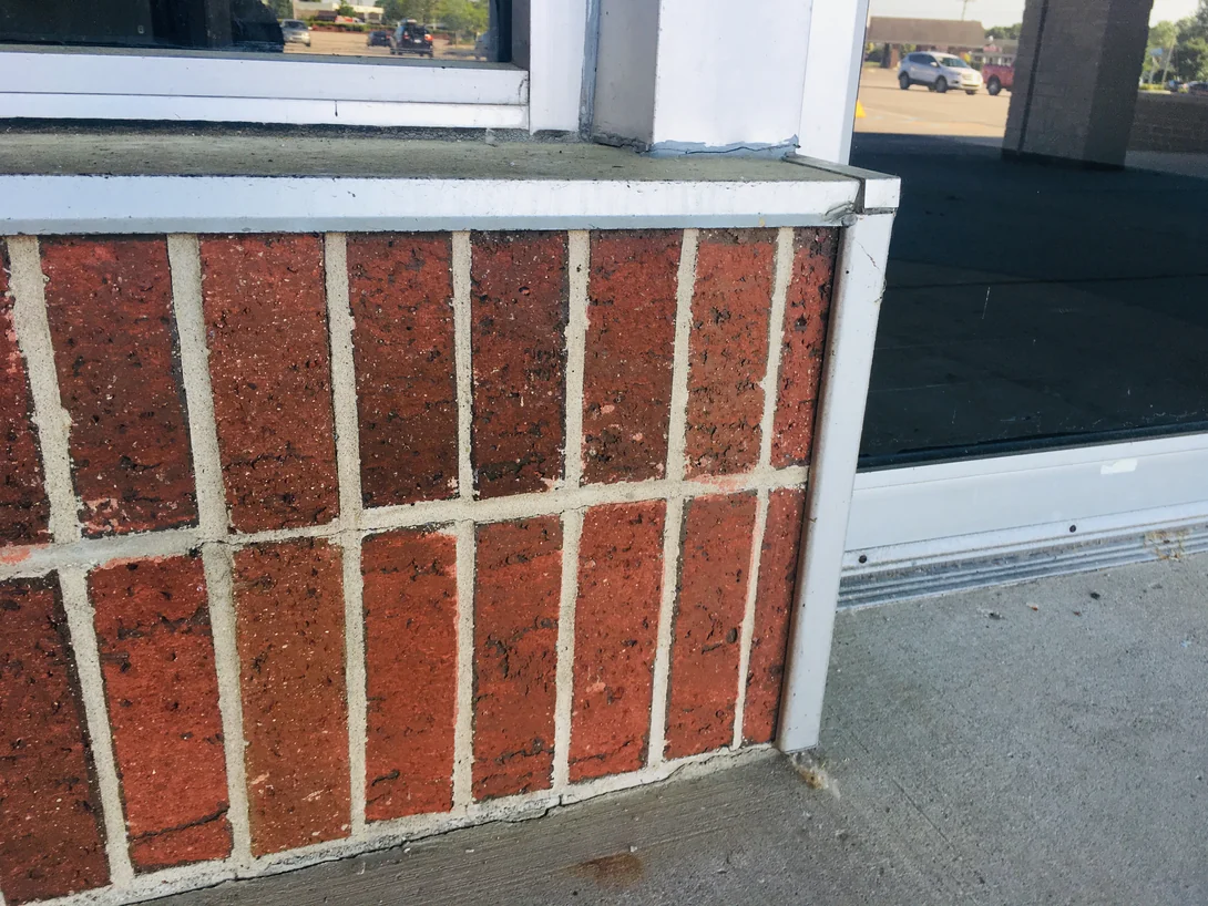 Close view of a low brick sill wall under a shopfront window in 2019, the units an even red with pale mortar joints and a cast stone cap