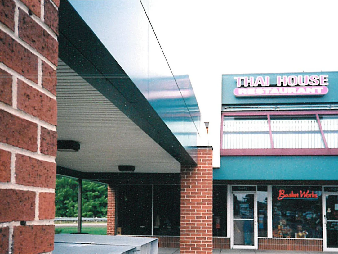 The covered walkway in 1998, a dark flecked brick pier in the foreground and a ladder standing against a smoother red pier by the shopfronts